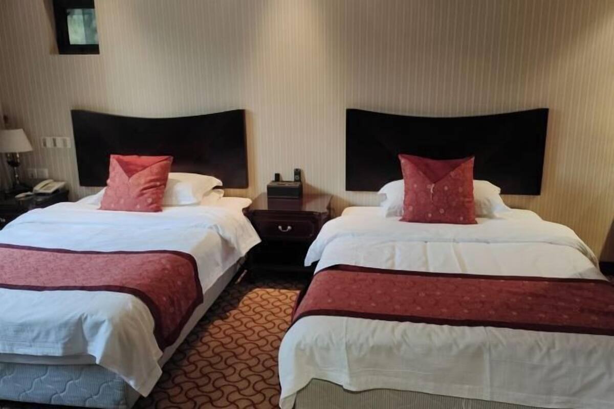 Habitación de hotel con dos camas, cada una con cabecera, mesita de noche, lámpara y teléfono.