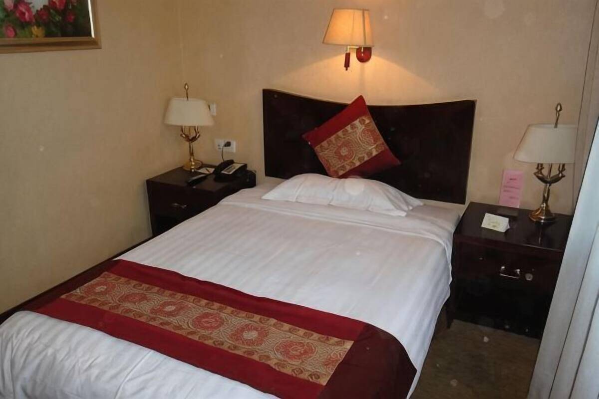 Una habitación de hotel con una cama, dos mesitas de noche, una lámpara, un teléfono y un tocador.