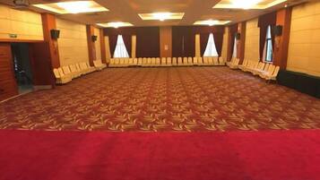 A large conference room with a patterned carpet, rows of chairs, and a red carpet border.