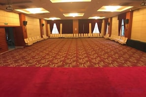 Une grande salle de conférence dotée d’un tapis à motifs, de rangées de chaises et d’une bordure de tapis rouge.