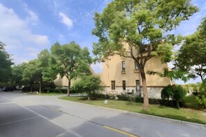 Un bâtiment à la façade beige, un parking et des arbres.