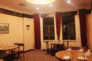 Un espace repas avec des tables et des chaises rondes, un tableau accroché au mur et une fenêtre avec des rideaux.