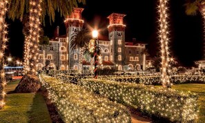 Un grand bâtiment illuminé, doté de nombreuses tours et d’un jardin bien éclairé.
