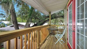 A wooden deck with a table and chairs, a red door, and a covered area with a ceiling. - Guesthouse w/ Balcony · Walk to Downtown · Bikes (St Augustine)