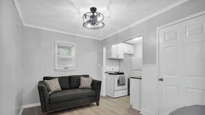 A modern kitchen with white cabinets, a stove, and a refrigerator. There is a gray sofa with patterned pillows in the living area. - Guesthouse w/ Balcony · Walk to Downtown · Bikes (St Augustine)