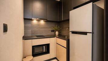 A modern kitchen with dark cabinetry, a built-in microwave, a stainless steel refrigerator, and a small trash bin.