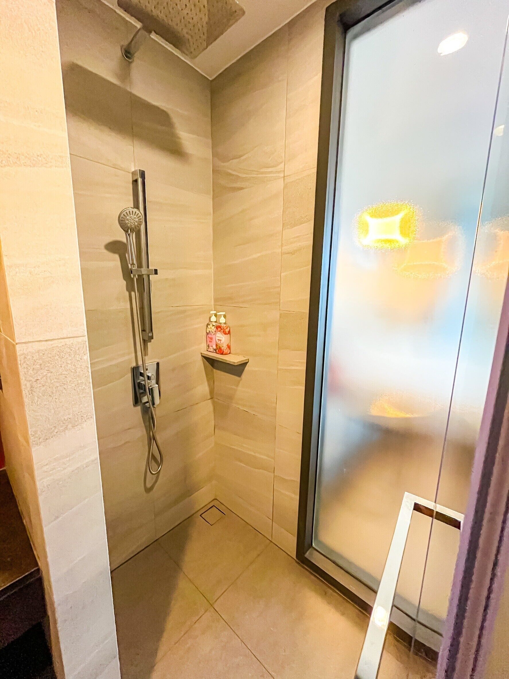 A small, modern shower room with a glass door, a handheld showerhead, and a soap dispenser on a shelf.