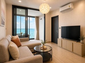 A modern living room with a sofa, a television, a coffee table, and a view of the ocean. - The Edge central pattaya  (Pattaya)