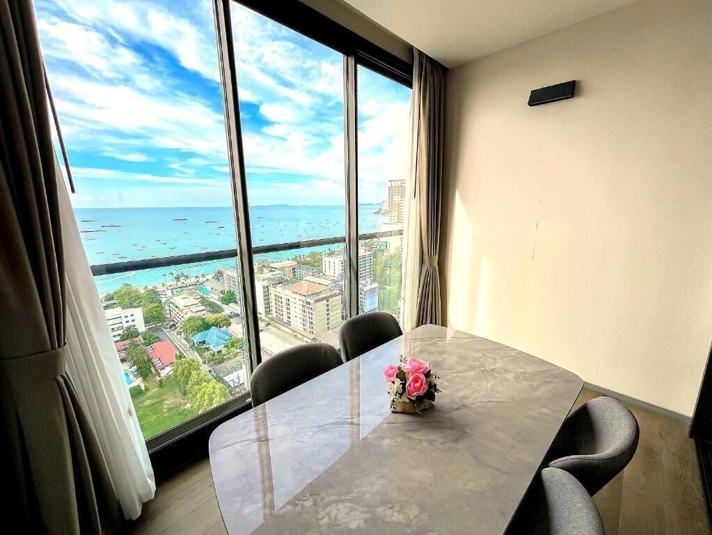 A room with a large window, a table with chairs, and a vase with flowers.