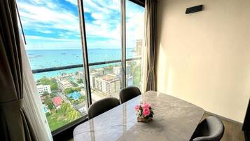 A room with a large window, a table with chairs, and a vase with flowers.