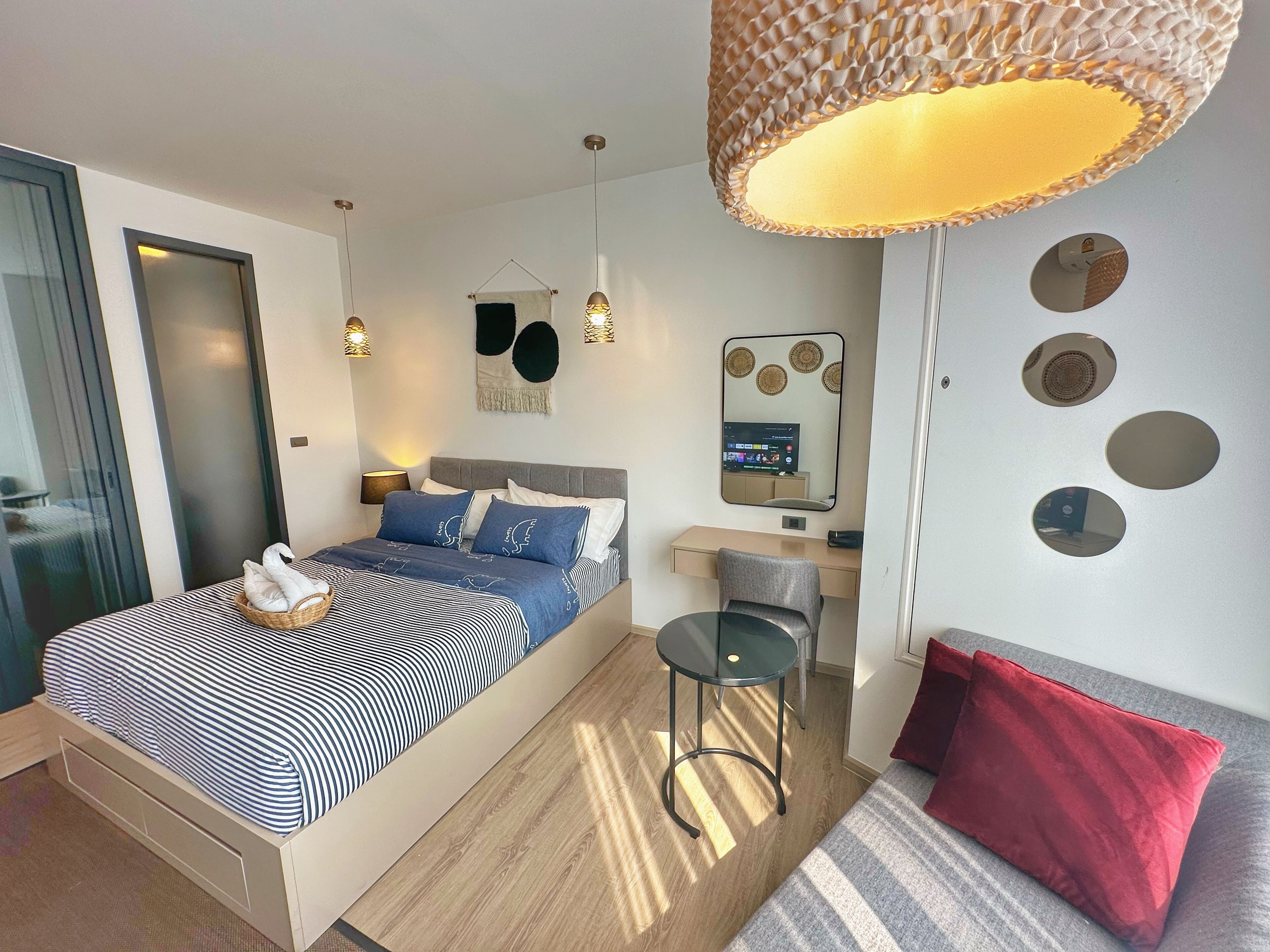 A modern bedroom with a bed, bedside table, lamp, mirror, and a small stool.