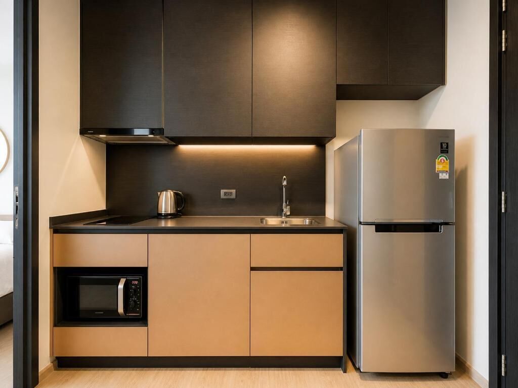 A compact kitchen with a built-in microwave, a stainless steel refrigerator, and a dark-colored cabinet above the counter.