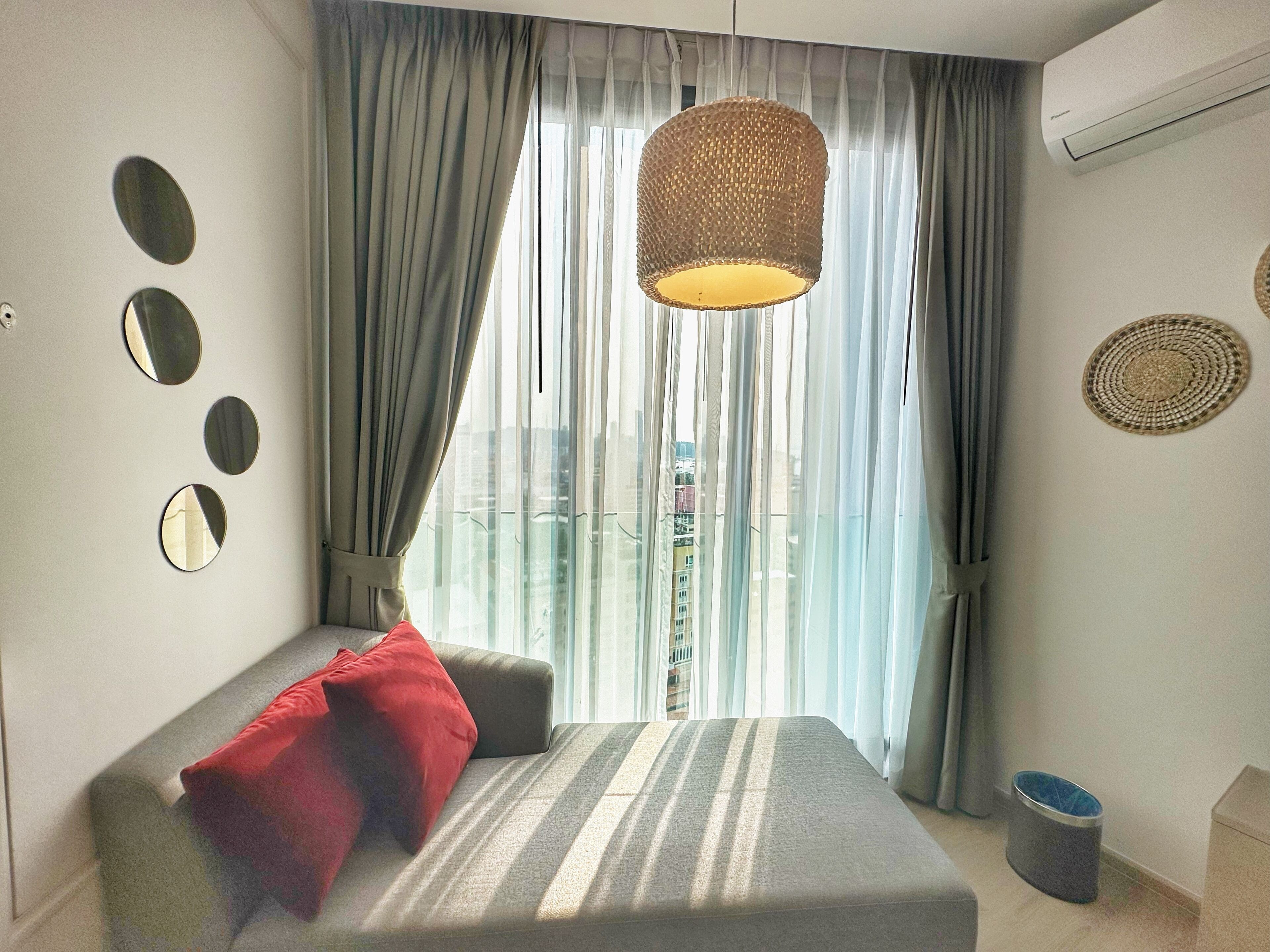 Une chambre à coucher avec un lit, un luminaire suspendu, une fenêtre avec des rideaux et une vue sur les bâtiments à l’extérieur.