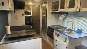 A compact kitchen with a microwave, oven, and sink. There is a bench and a small refrigerator. - Nice RV with AC in charming Holly Beach steps from the beach (Cameron)