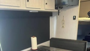 A compact kitchenette with a built-in stove, a small refrigerator, and a seating area with a table and bench. - Nice RV with AC in charming Holly Beach steps from the beach (Cameron)
