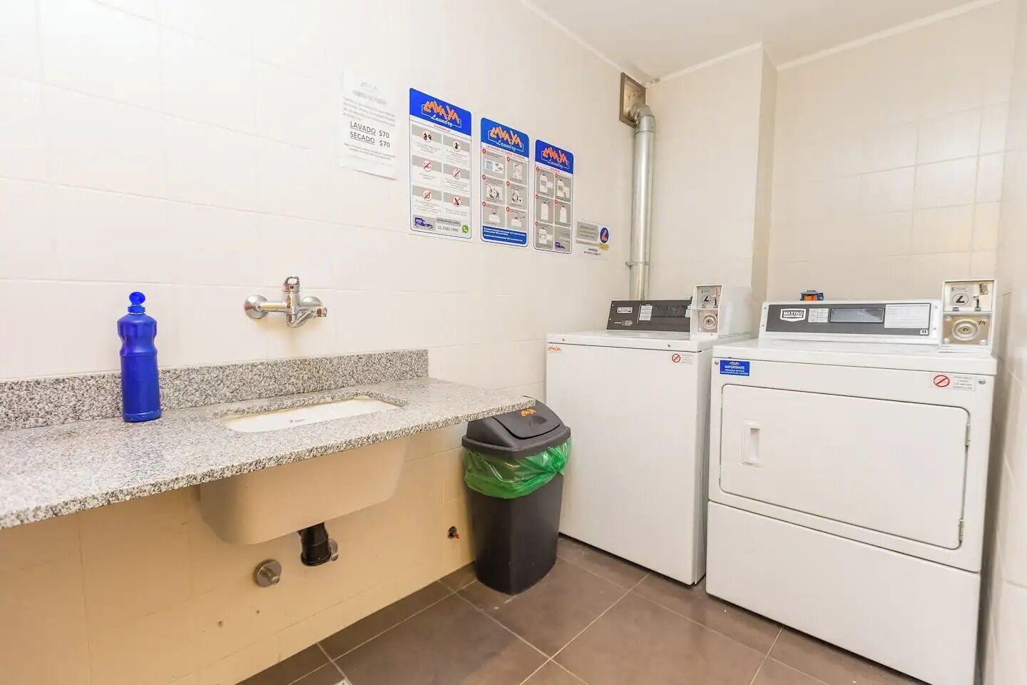 A small laundry room with a sink, a trash bin, and a washing machine.