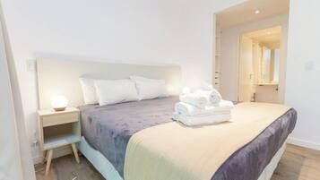 Una habitación de hotel moderna con una cama grande, una mesita de noche y un buró.