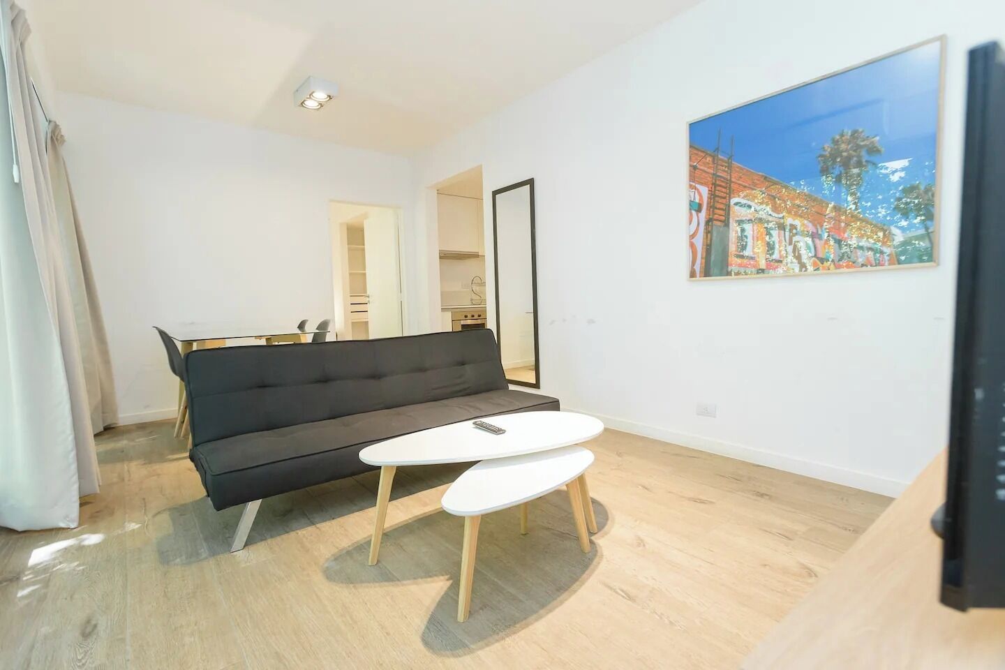 A modern living room with a black sofa, a white coffee table, and a painting on the wall.