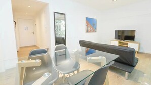 A modern living room with a glass table, two grey chairs, a black sofa, a television on a wooden cabinet, and a painting on the wall. - Apartamento de 2 Ambientes en Belgrano (Buenos Aires)