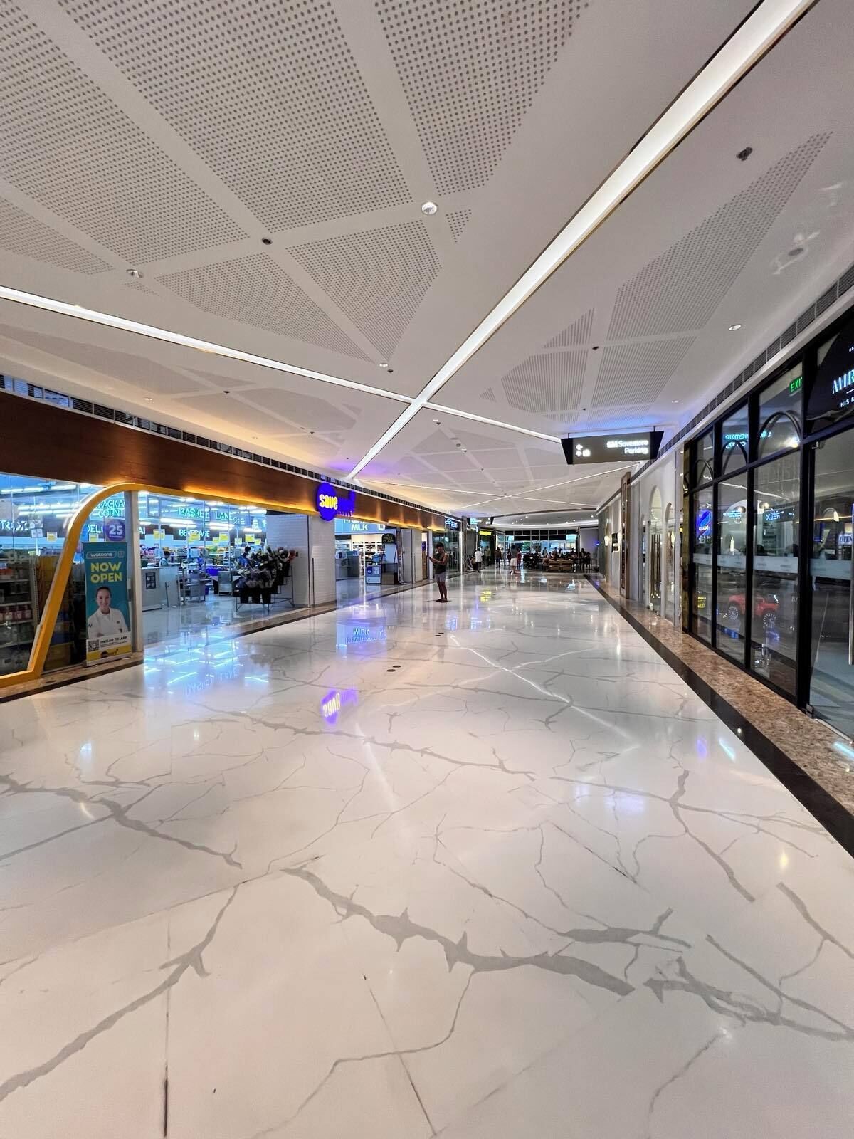 A spacious corridor with a polished marble floor, modern ceiling design, and glass storefronts.