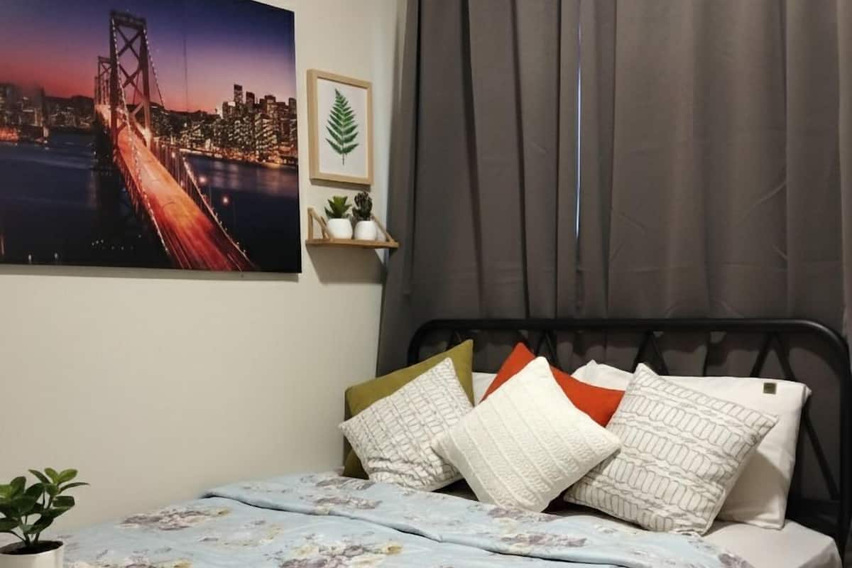 A bedroom with a bed, a potted plant, a framed picture, and a curtain.