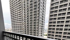 Un balcon avec vue sur des immeubles de grande hauteur, un espace verdoyant et une route.