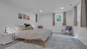 Un dormitori modern amb un llit gran, una taula auxiliar, una cadira i una finestra amb cortines.