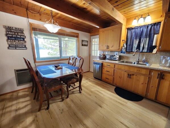 Interior de una cabaña de madera con una mesa de comedor, sillas, una zona de cocina y un cartel que anuncia actividades como pesca y lectura.