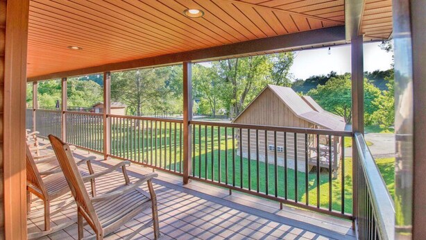 A covered porch with wooden flooring and a railing, overlooking a green lawn and a wooden cabin. - Cozy Log Cabin Retreat w/ Pool | Pigeon Forge TN (Pigeon Forge)