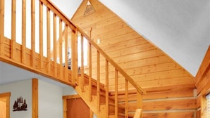 A wooden staircase leading to a loft bedroom with a small dining area below. - Cozy Log Cabin Retreat w/ Pool | Pigeon Forge TN (Pigeon Forge)