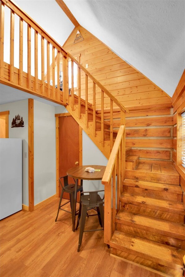 Una escalera de madera que sube a un dormitorio en un altillo, con un pequeño comedor abajo.