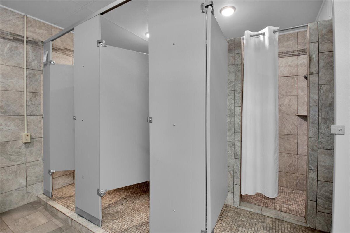 Een openbaar toilet met drie cabines, een douchegedeelte en een betegelde vloer.