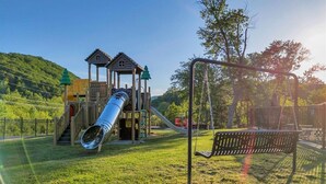 A playground with a slide and swings, surrounded by grass and trees. - Charming 1BR Smoky Mtn Cabin w/ Pool Access (Pigeon Forge)