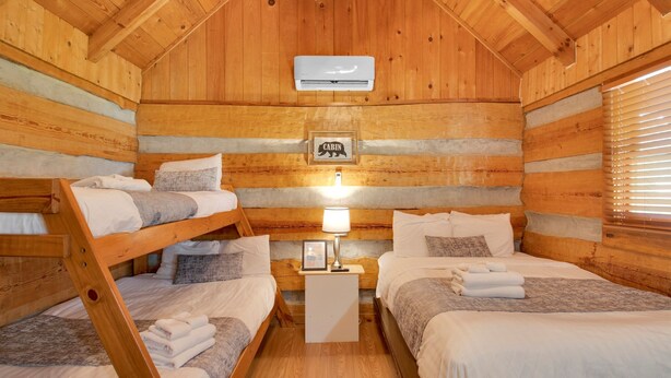 Una habitación tipo cabaña con literas, un cuadro en la pared y una mesita de noche con una lámpara.