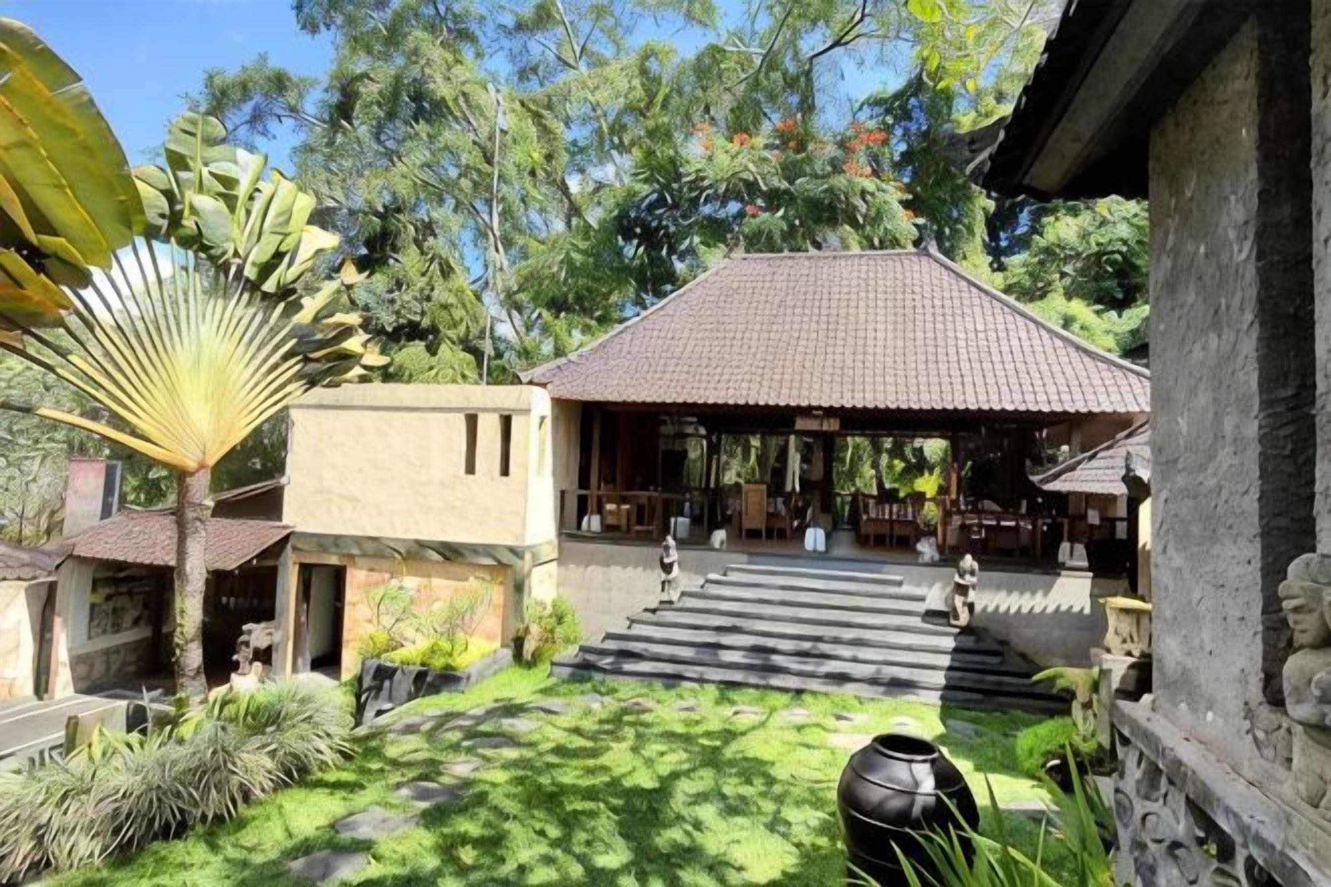 A traditional building with a tiled roof, a stone pathway leading to the entrance, and a lush garden with various plants.