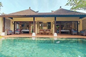 A poolside area with a covered seating area, a pool, and a building with a tiled roof.