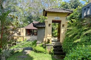 A traditional building with a tiled roof, a stone pathway leading to the entrance, and lush greenery surrounding the area.