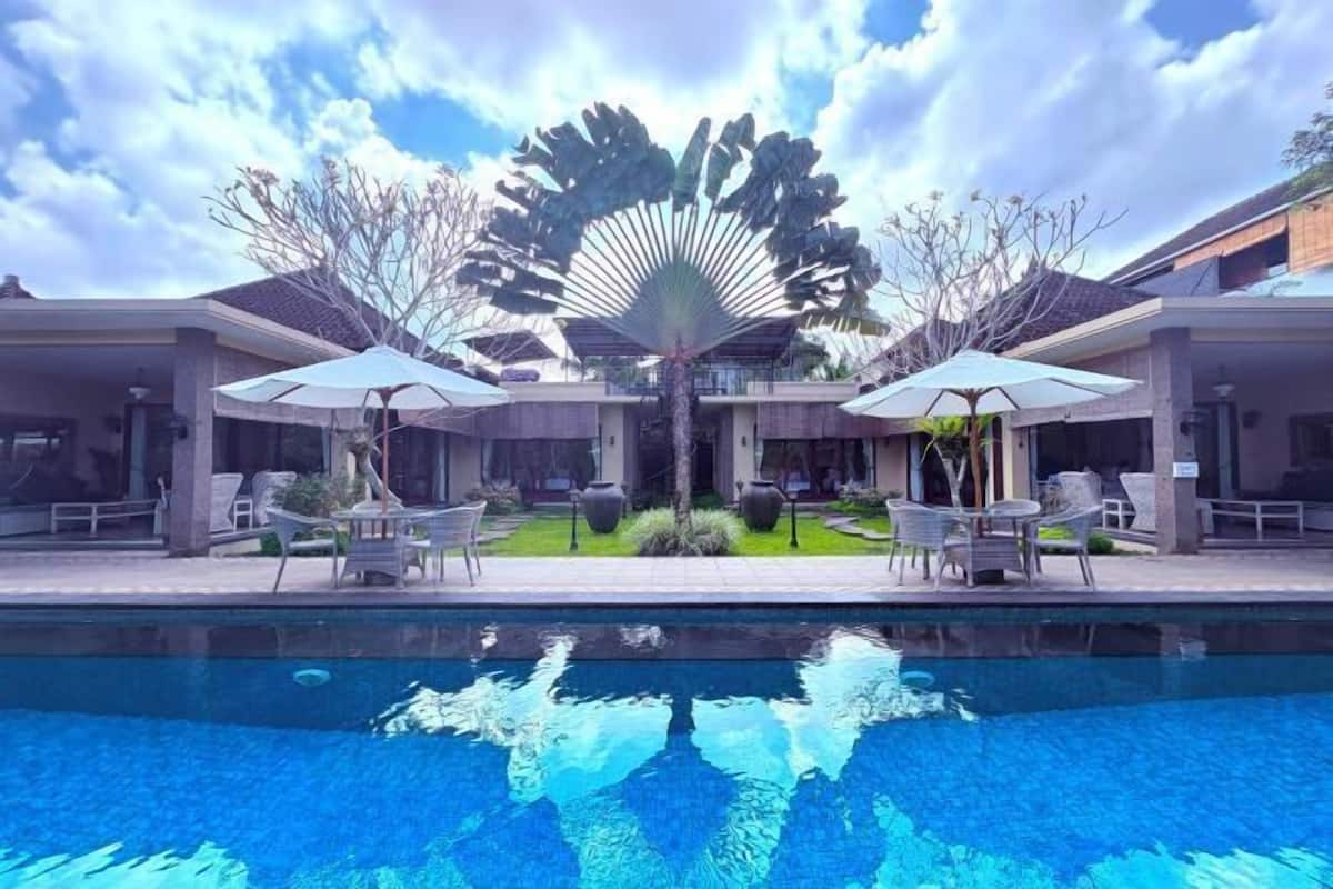 A swimming pool with lounge chairs and umbrellas, surrounded by a building with a modern design.
