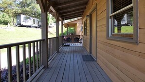 A wooden porch with a bench, a covered area, and a view of a grassy area with a trailer in the background. - Cozy Pigeon Forge Cabin w/ Mountain Views (Pigeon Forge)