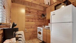 A compact kitchen with wooden walls, a white refrigerator, a stove, and a small countertop. - Cozy Pigeon Forge Cabin w/ Mountain Views (Pigeon Forge)