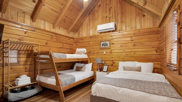A cabin-style room with wooden walls and a sloped ceiling. There are two bunk beds and a single bed. A sign on the wall reads "CABIN." - Cozy Pigeon Forge Cabin w/ Mountain Views (Pigeon Forge)