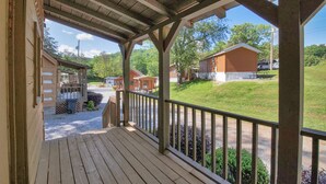 A wooden porch with a view of a grassy area and small cabins.