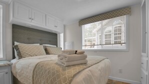 A neatly made bed with a patterned bedspread, a headboard, and a window with blinds. - Charming 1BR Cottage with Loft near Dollywood (Pigeon Forge)