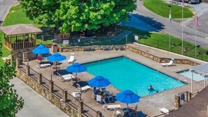 A swimming pool with lounge chairs and umbrellas, surrounded by a stone wall and a gazebo. - 1BR Cottage Retreat with Loft near Dollywood (Pigeon Forge)