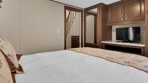 A bedroom with a bed, a TV on a stand, wooden cabinets, and a door leading to another room. - 1BR Cottage Retreat with Loft near Dollywood (Pigeon Forge)