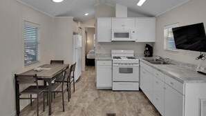 Una cocina compacta con armarios blancos, un microondas, una estufa y un televisor de pantalla plana montado en la pared.