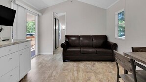 Una habitación con ventilador de techo, un sofá de cuero marrón, una mesa de comedor de madera y un armario blanco.