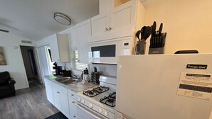 A modern kitchen with white cabinets, a gas stove, a microwave, and a refrigerator. There is a black mat on the floor, and a knife set is visible on the refrigerator. - Pigeon Forge 2BR Cottage w/ King & Queen Beds (Pigeon Forge)