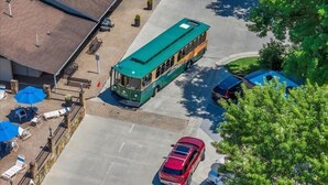 A green bus parked in front of a building with a sloped roof, a red car in the foreground, and a tree to the right. - Pigeon Forge 2BR Cottage w/ King & Queen Beds (Pigeon Forge)