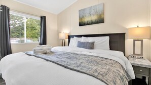 Una habitación de hotel con una cama grande, dos lámparas de noche, un cuadro en la pared y un ventanal con cortinas.